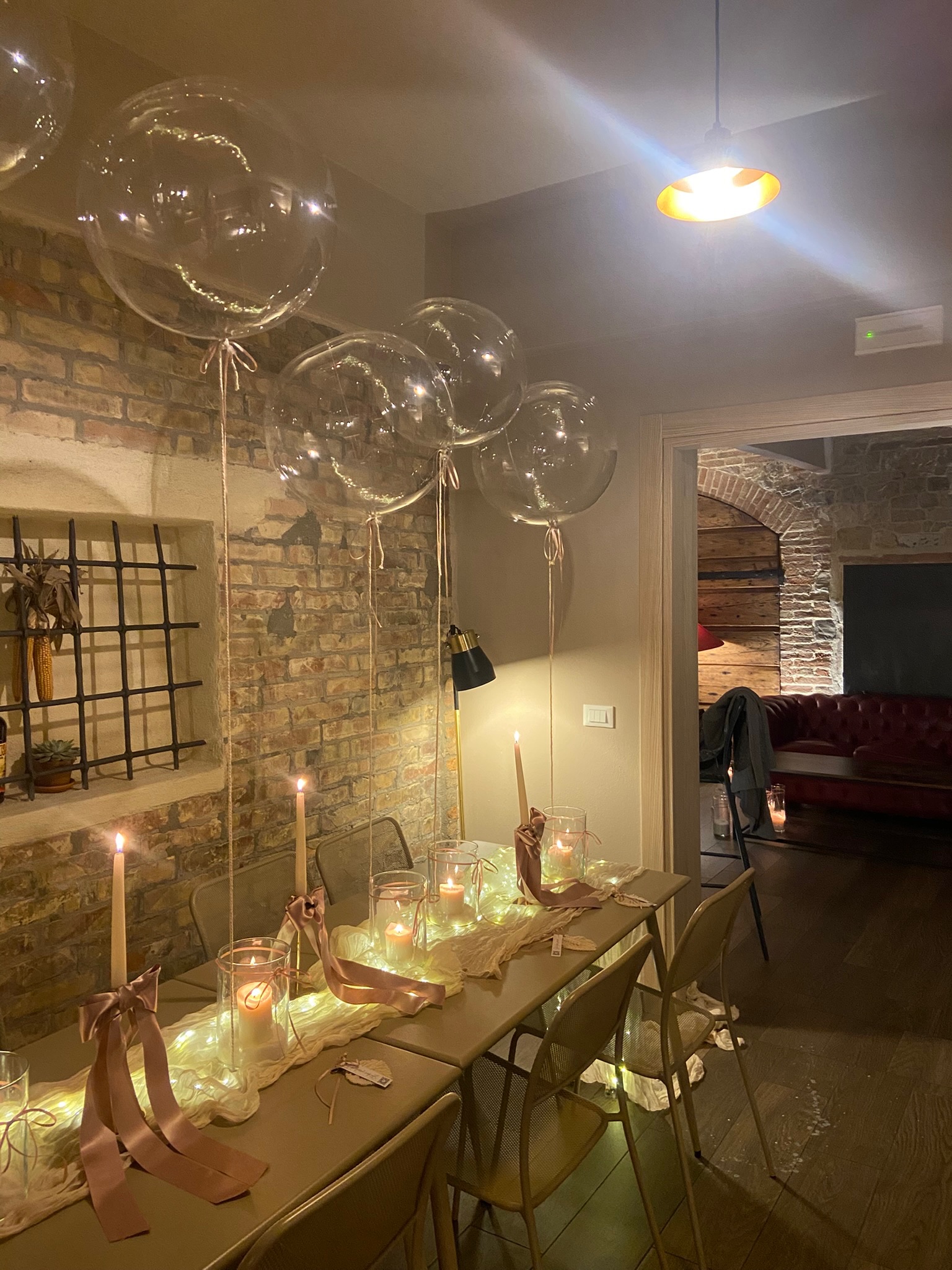 Sala con mattoni a vista, palloncini trasparenti, candele e nastri rosa antico