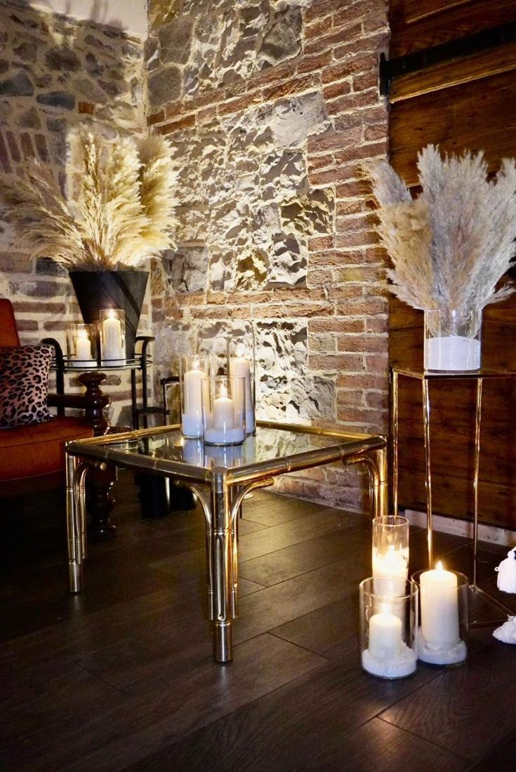 Sala con muro in pietra, candele e composizioni di pampas